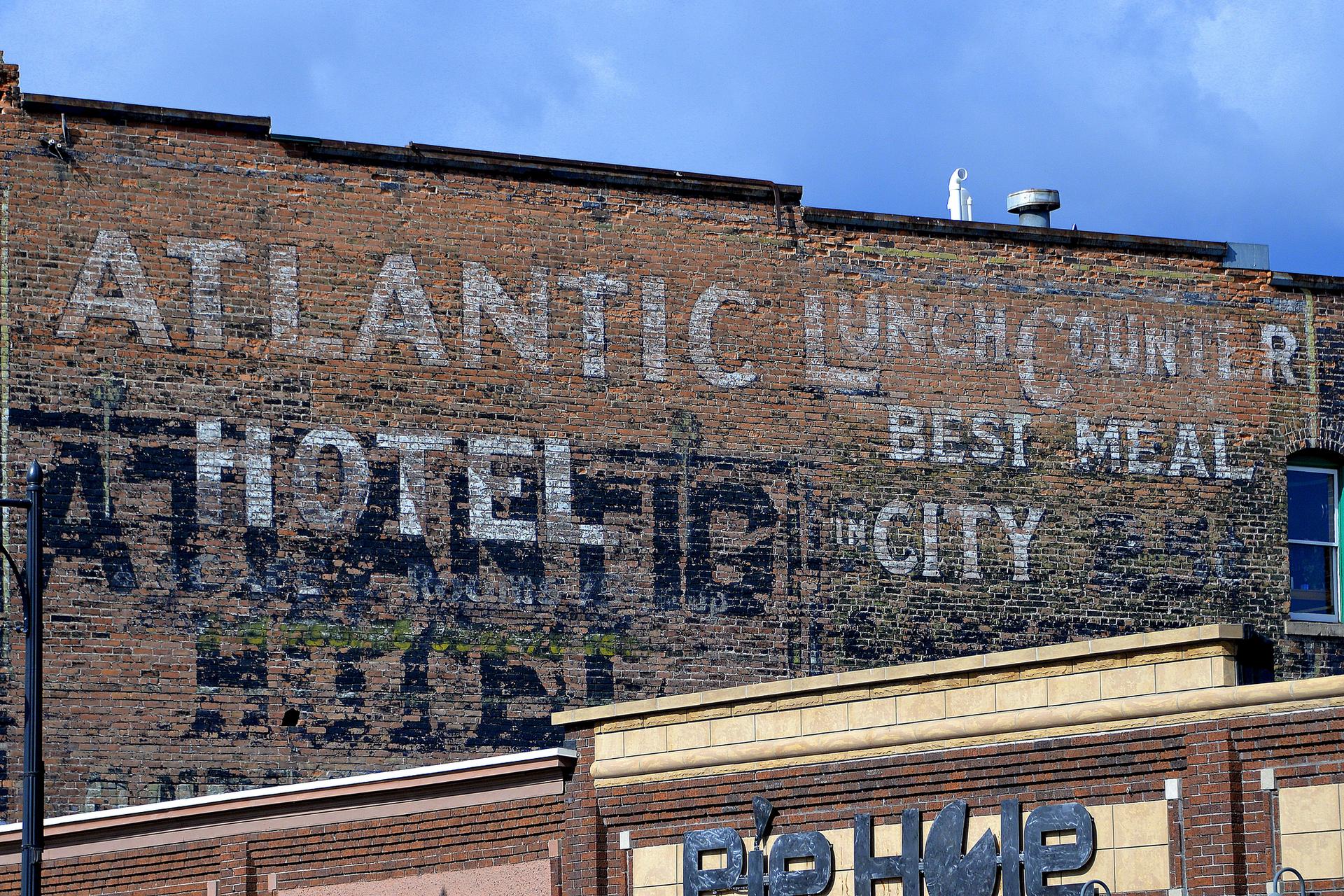 Faded advertisements on an old brick building under a partly cloudy sky.
