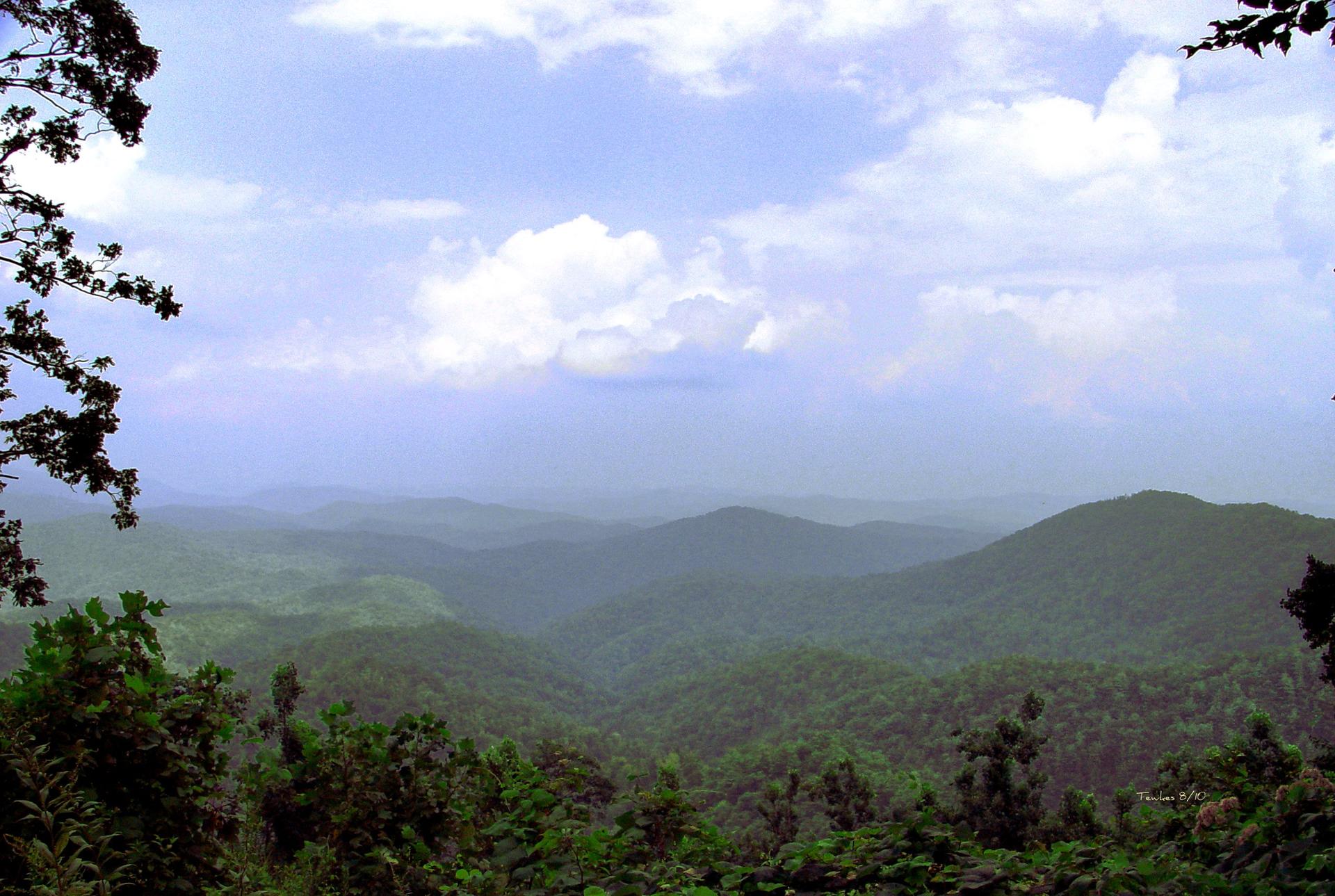 Expansive view of green, forested mountains under a dramatic, cloudy sky.