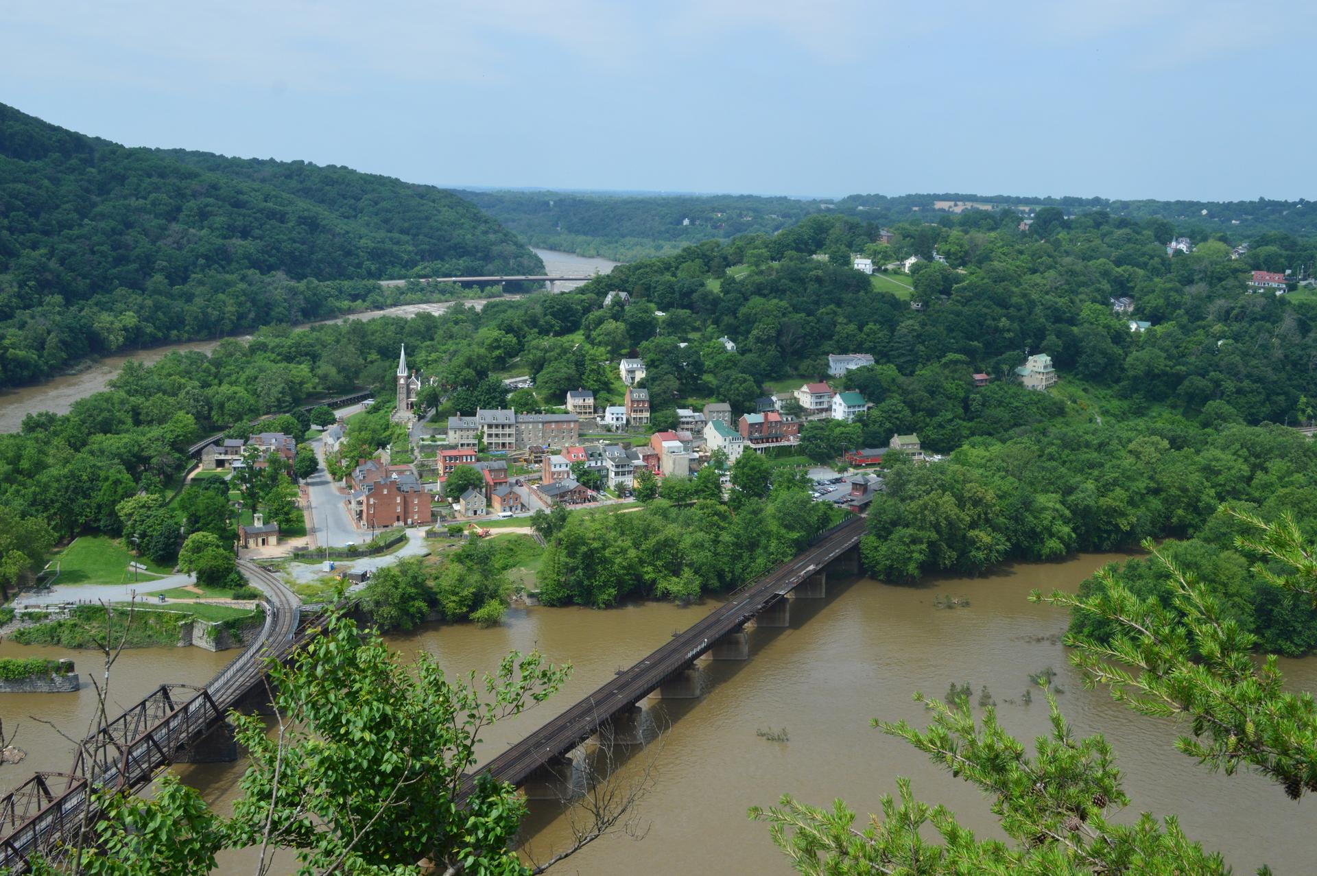 Overcast view of a river, town, and bridges surrounded by green hills.
