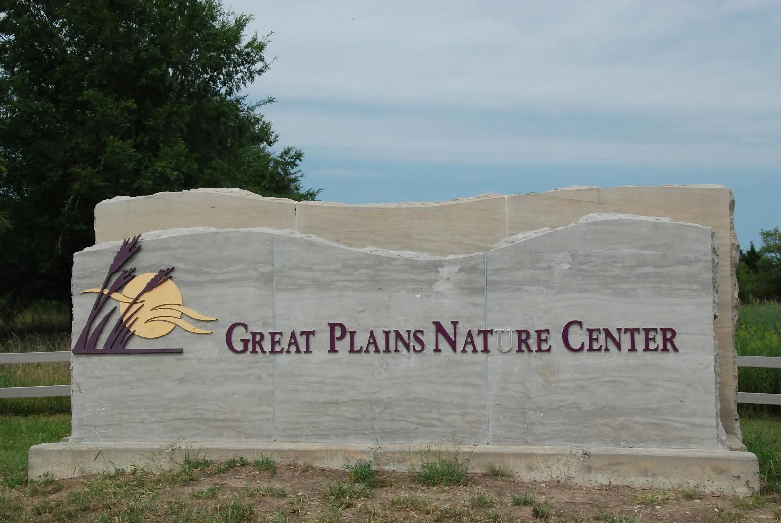 Large stone sign with nature center text and logo under an overcast sky. - Great Plains Nature Center Loop
