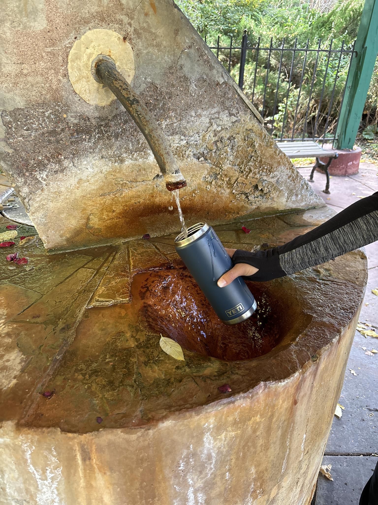 A person fills a blue water bottle from a stone spigot into a basin. - Intemann and Iron Mountain Trail Loop