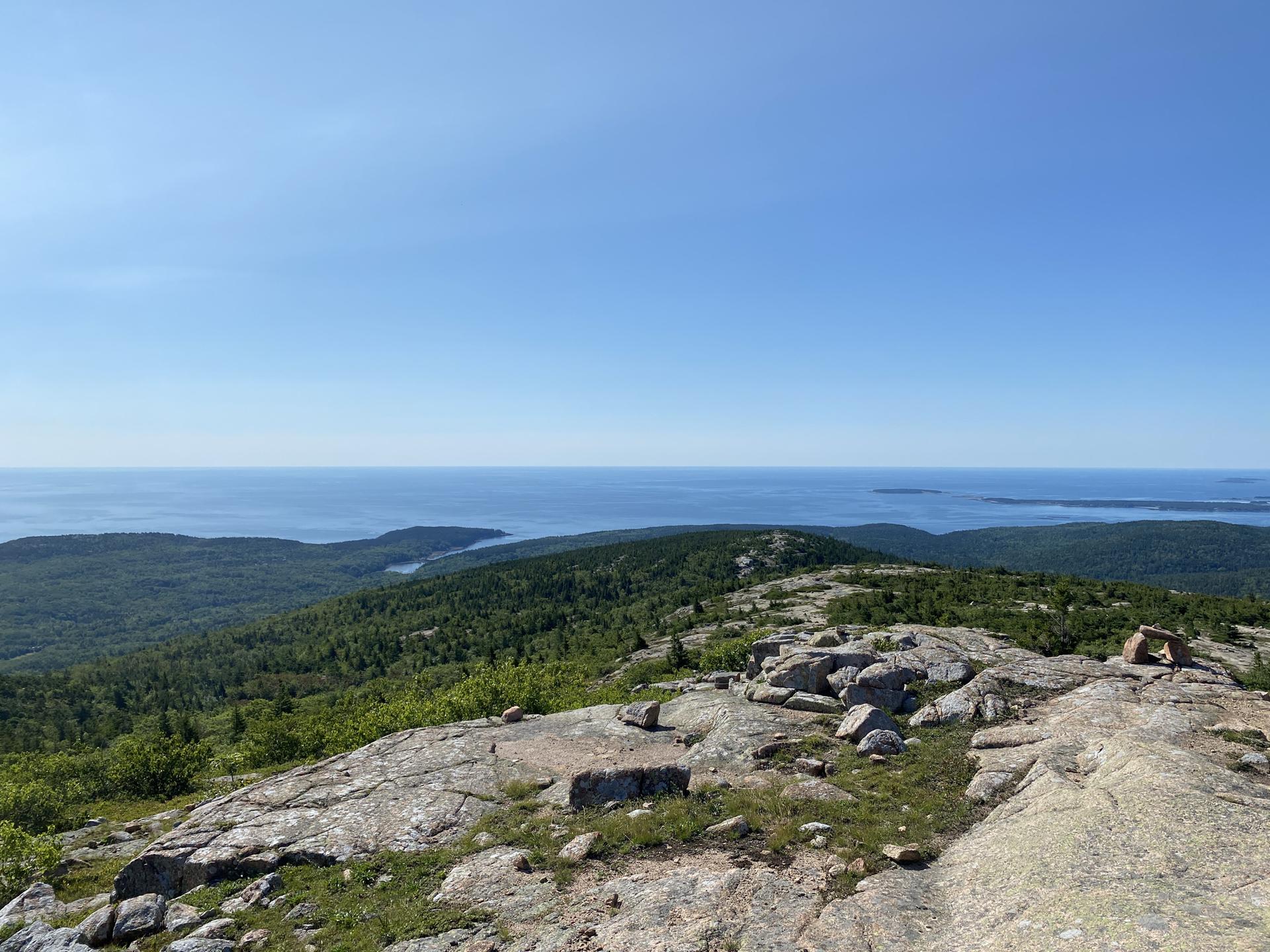 Expansive view from a rocky mountain peak towards the distant ocean, clear sky.