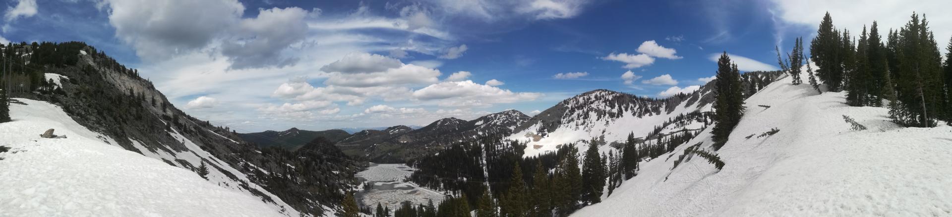 Panoramic view of snow-covered mountains and a partially frozen lake under a cloudy sky.