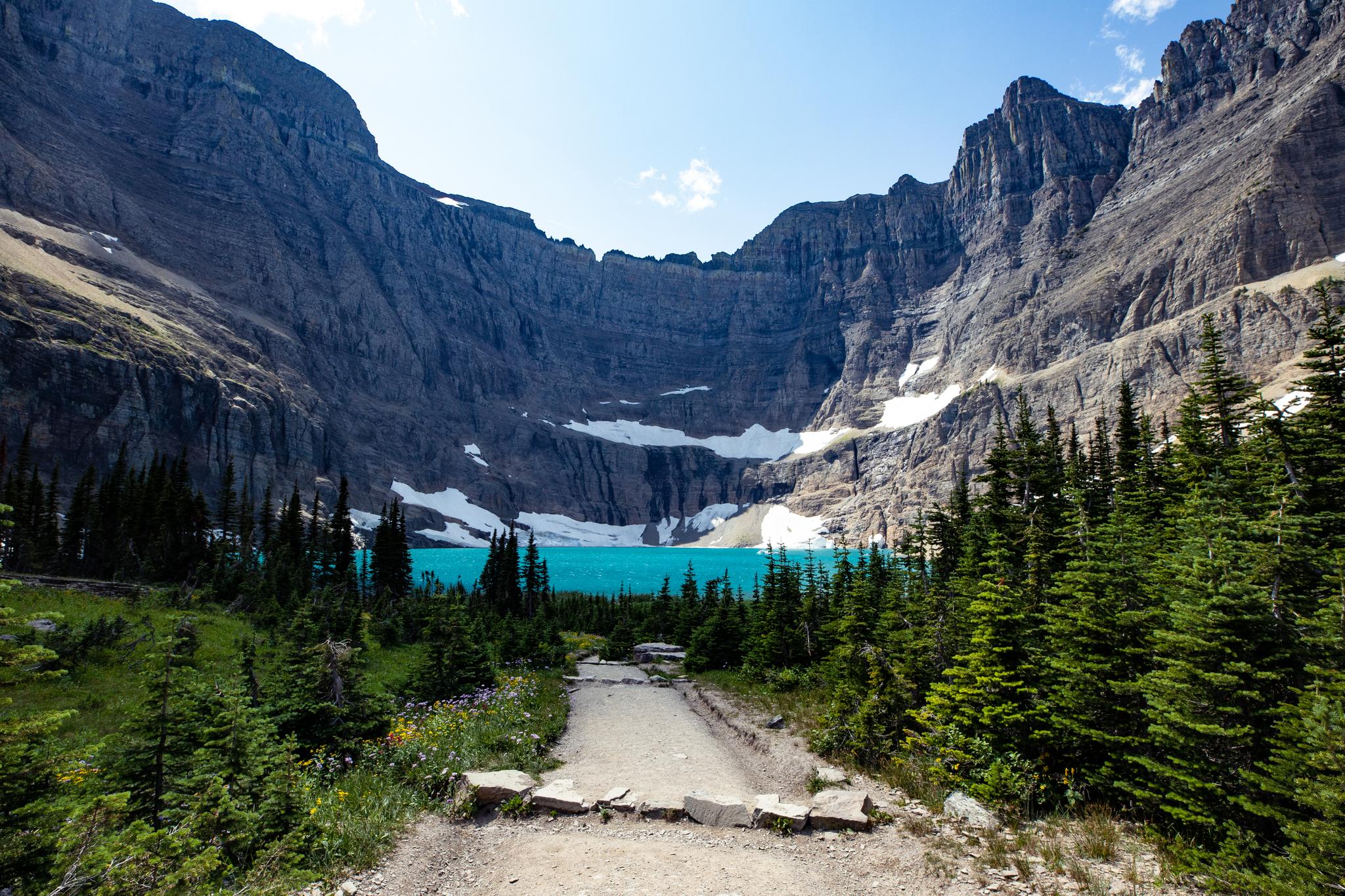 Path to a bright turquoise lake nestled among tall mountains and pines.