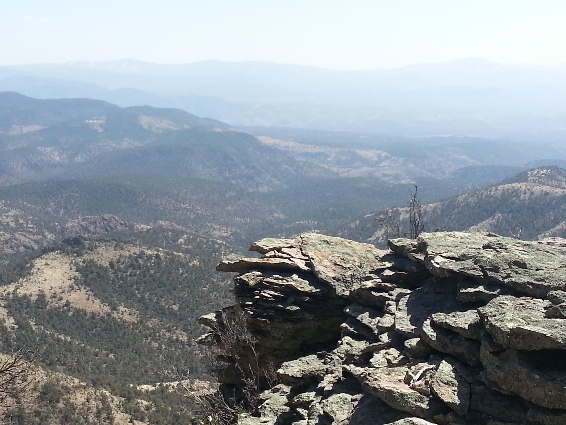 View from a rocky cliff overlooking hazy, forested mountain ranges.