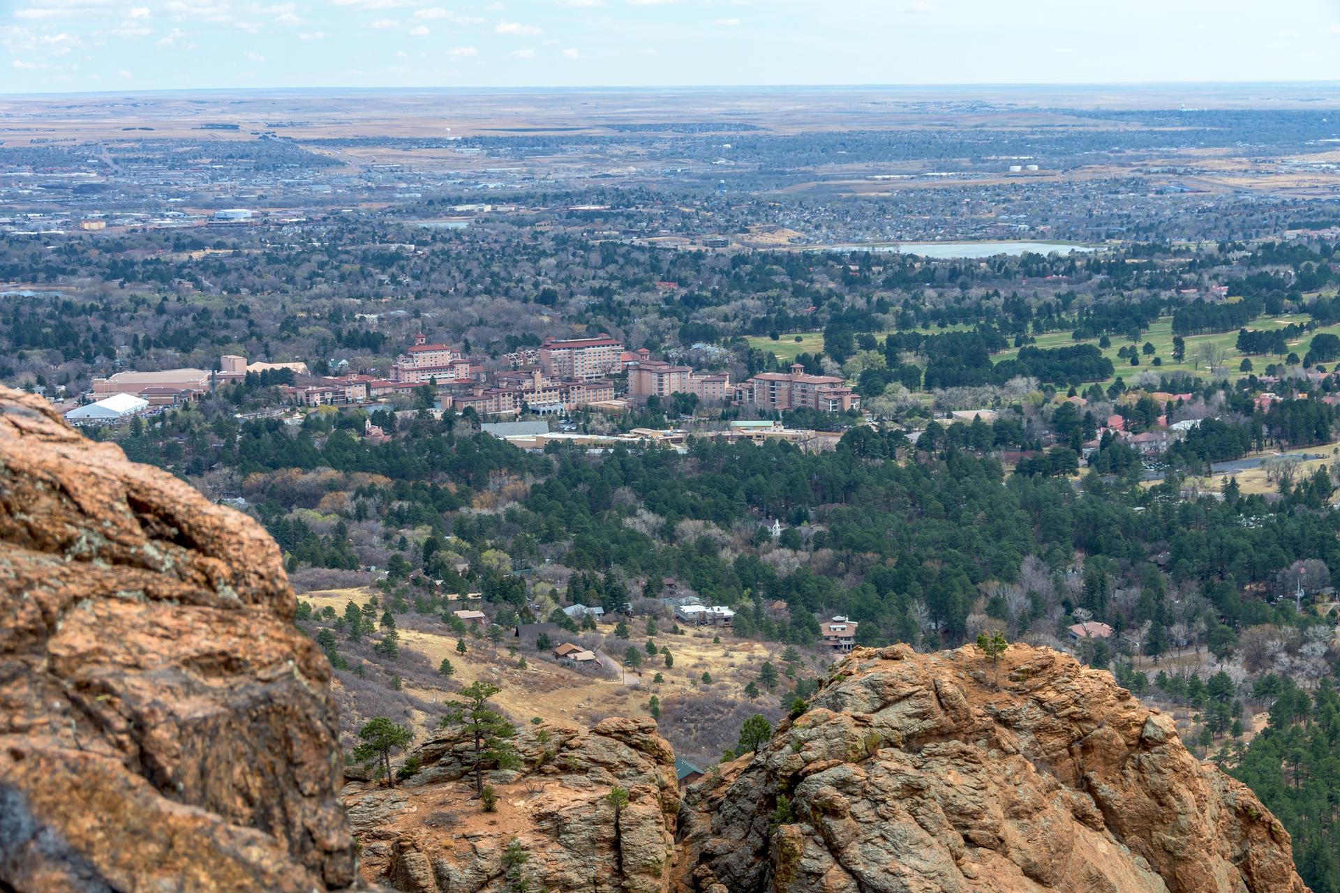 Panoramic view of a city nestled in a vast forested valley from rocky peaks.