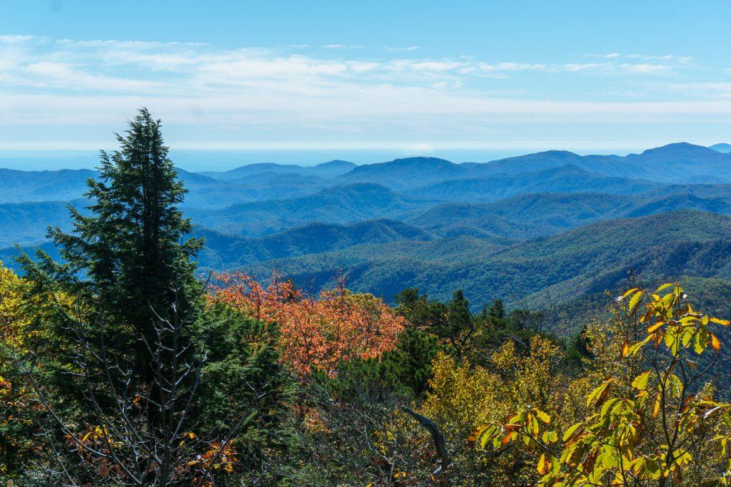 Vast blue mountain ranges under a clear sky, with colorful autumn trees foreground.