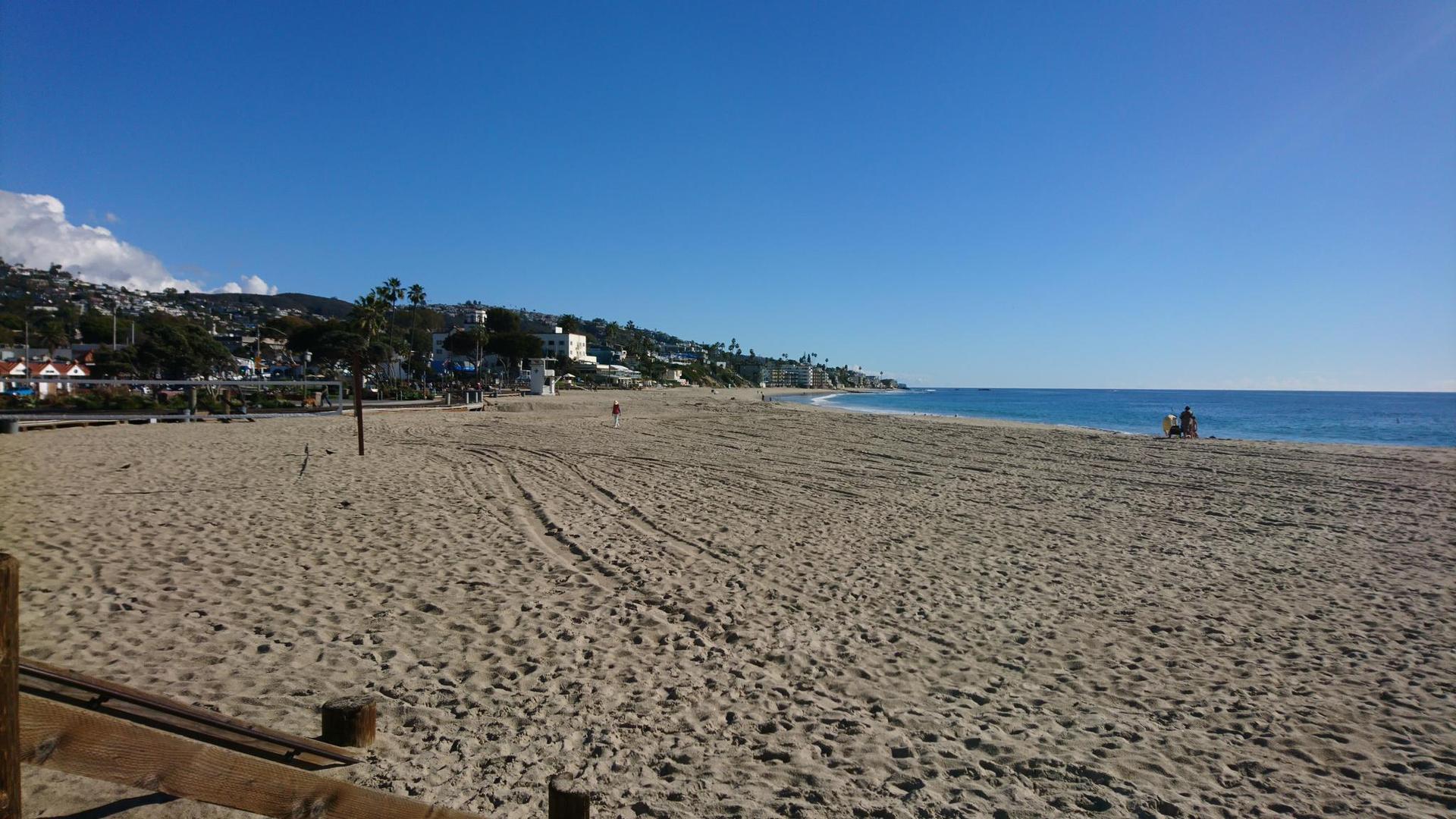 Expansive sandy beach with distant people and blue ocean under clear sky.