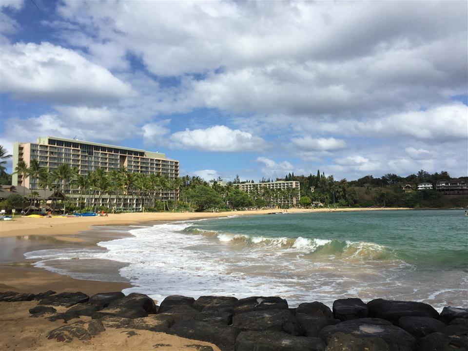Ocean waves on a sandy beach with large resort buildings under a cloudy sky.