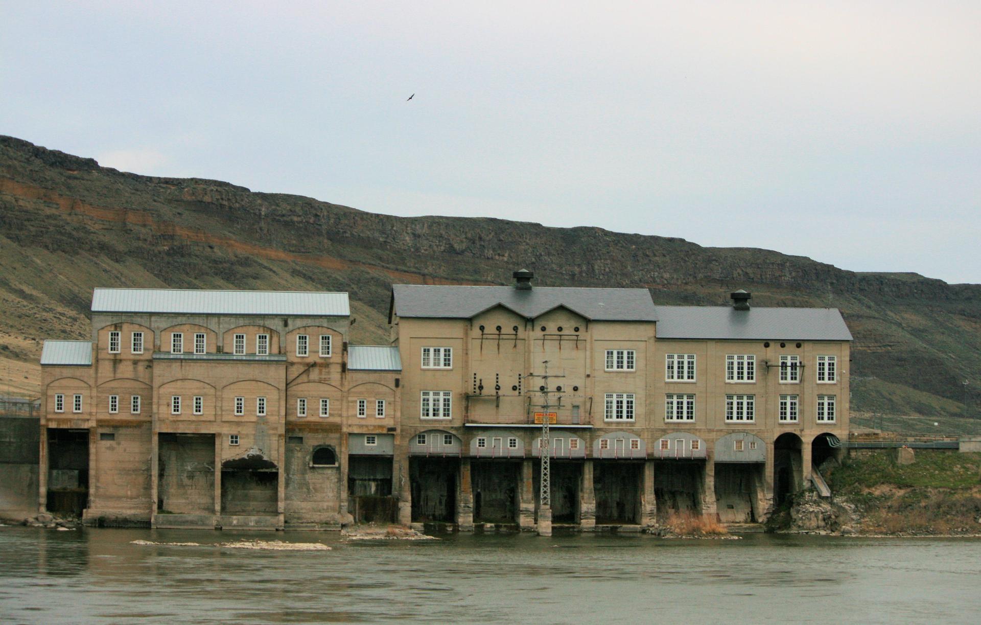 Large, old industrial building by a river under an overcast sky.