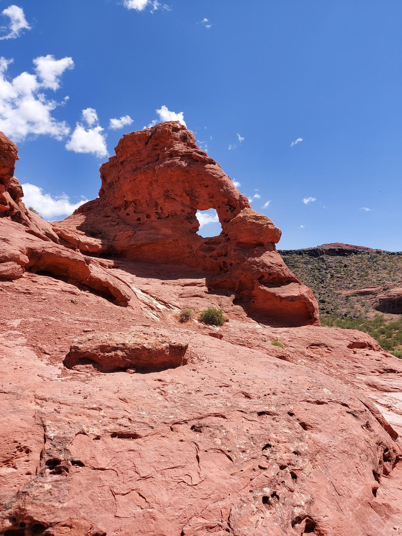 Red rock arch formation with a hole, under a bright blue sky.