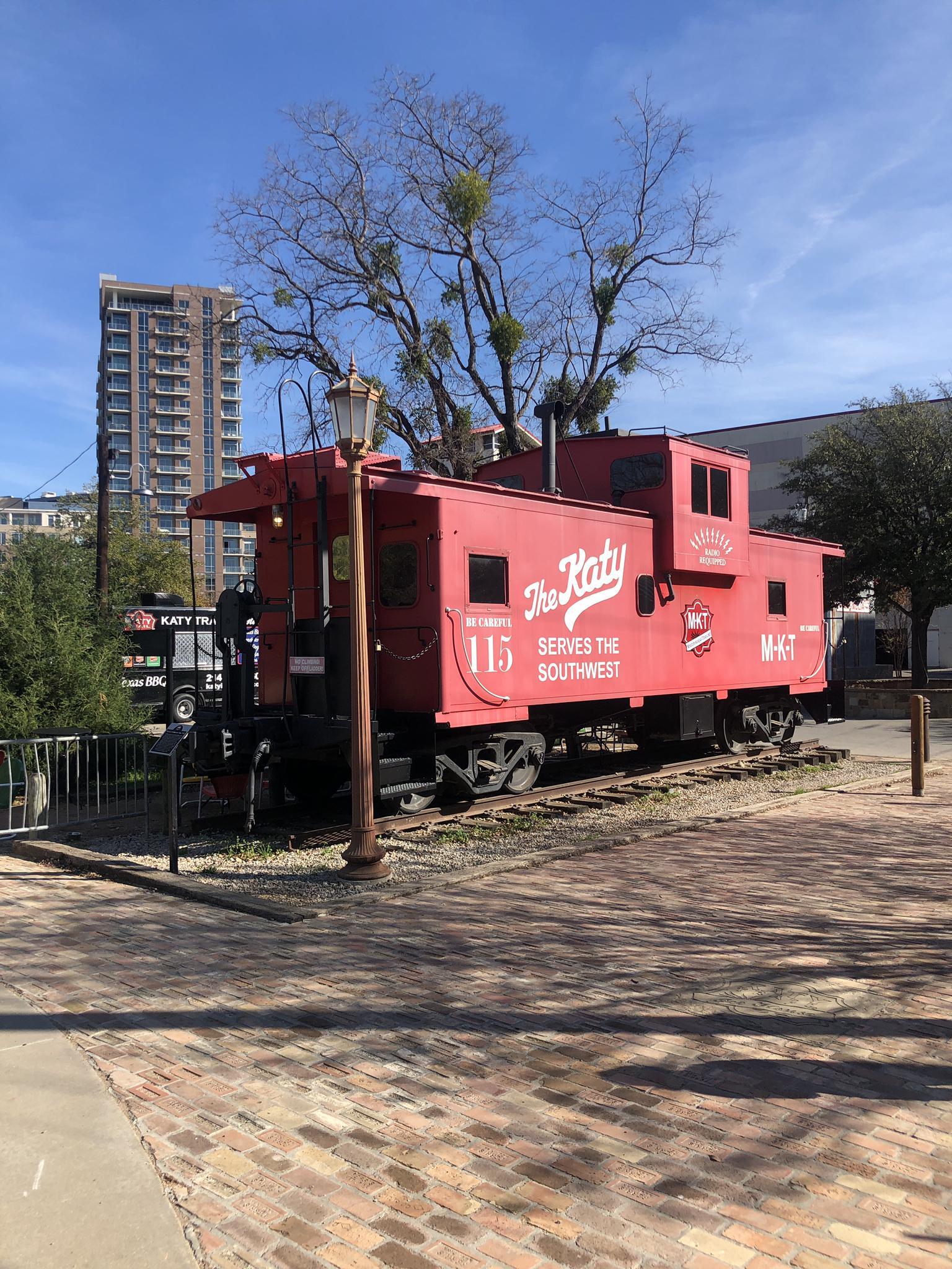 Bright red train caboose on tracks with a tall building behind.