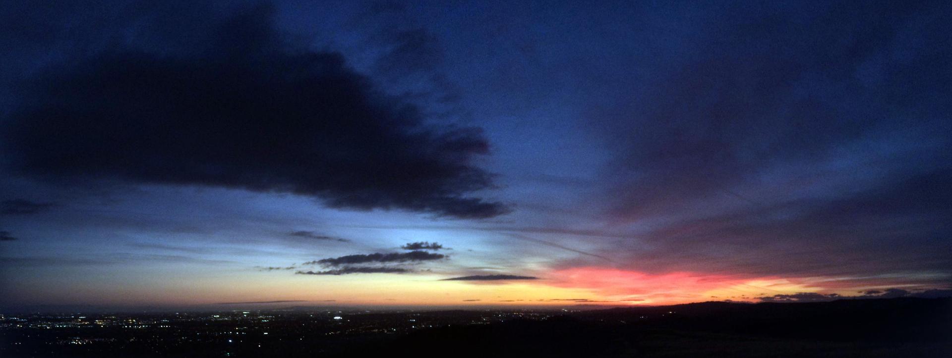 Dark clouds over a vibrant sunset sky with distant city lights.