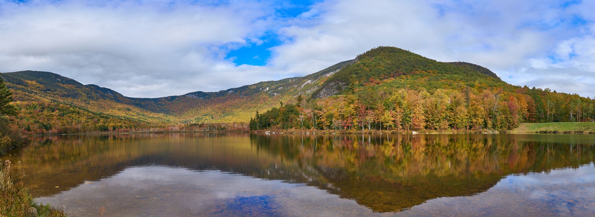 Calm lake reflecting autumn-colored mountains and trees under a cloudy sky. - Basin Trail