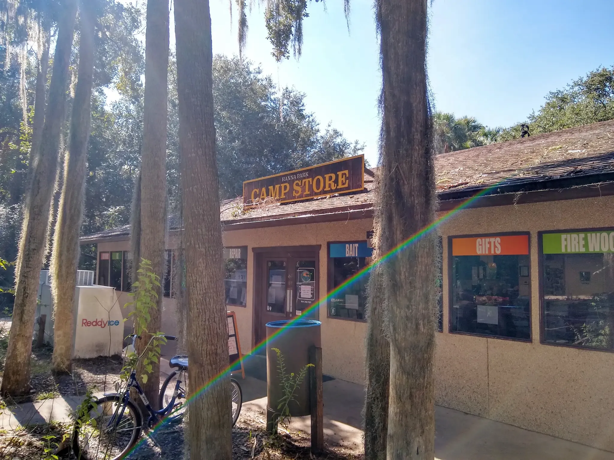 Sunny view of a camp store with tall trees and a parked bicycle. - East Coast Greenway (FL)