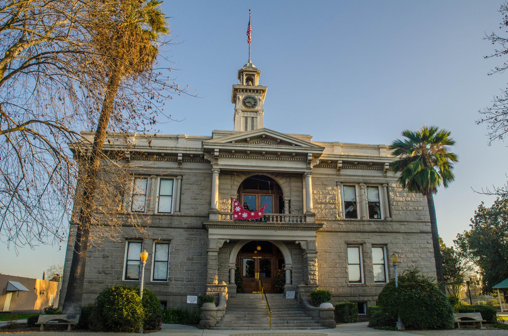 Grand stone building with a clock tower, surrounded by trees under a clear sky.