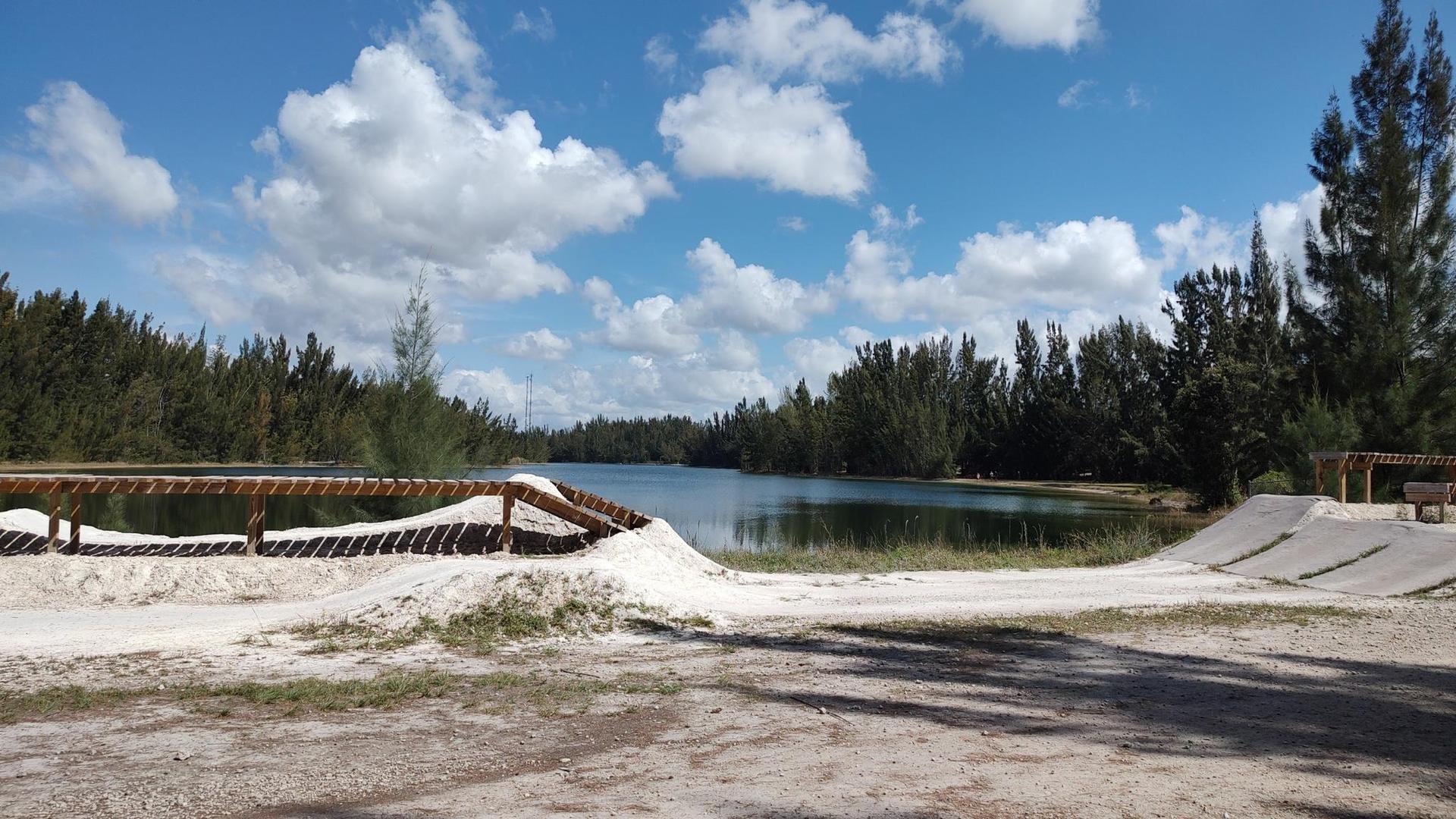 Sunny lake surrounded by pine trees and sandy recreational ramps.