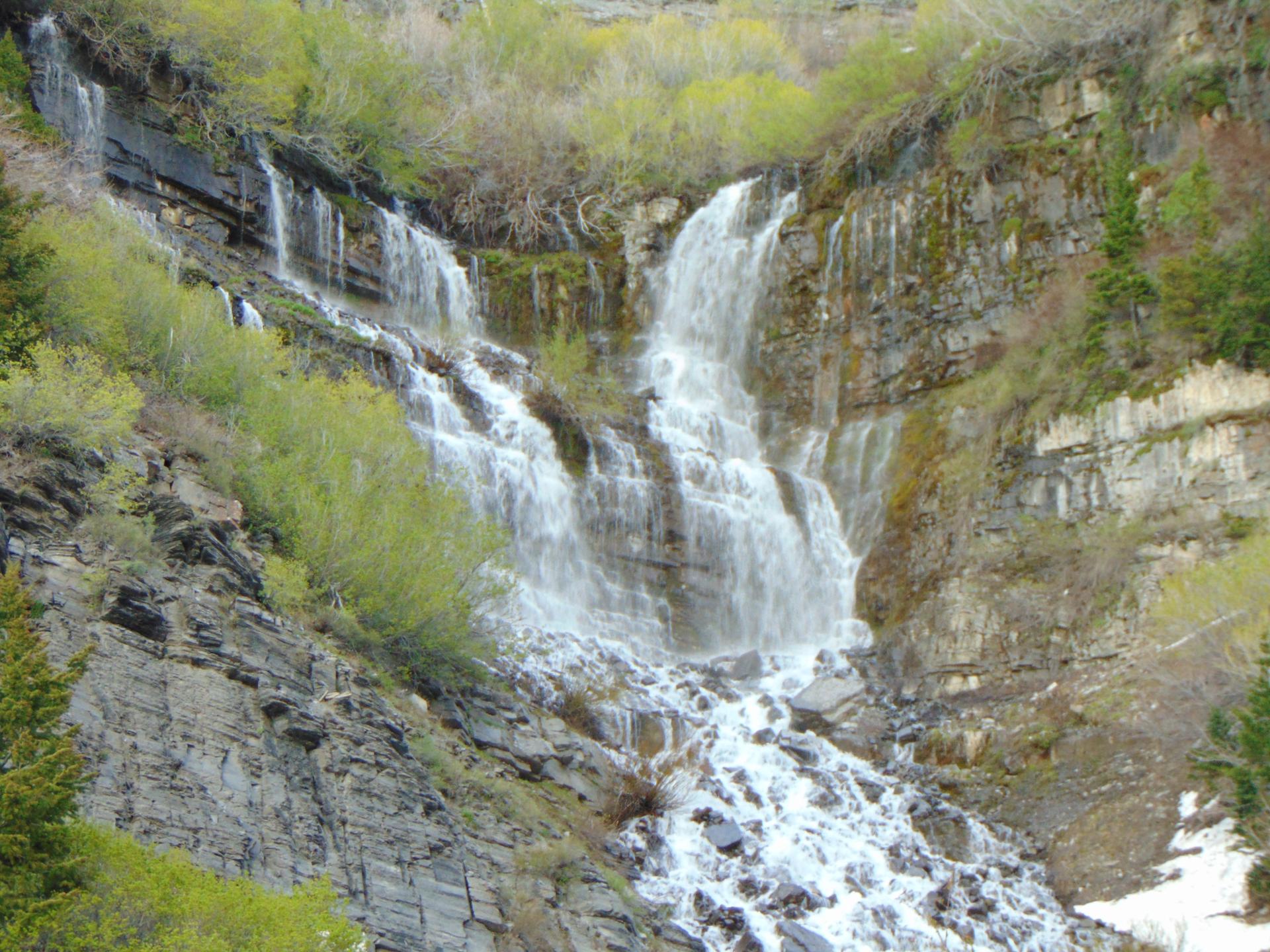 A multi-tiered waterfall cascades down a rocky, green hillside.