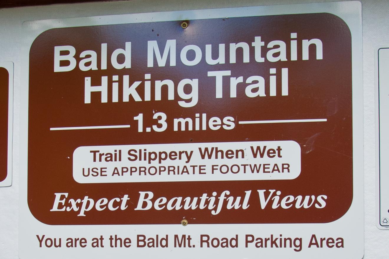 A brown hiking trail sign with white text, advising caution and promising views.