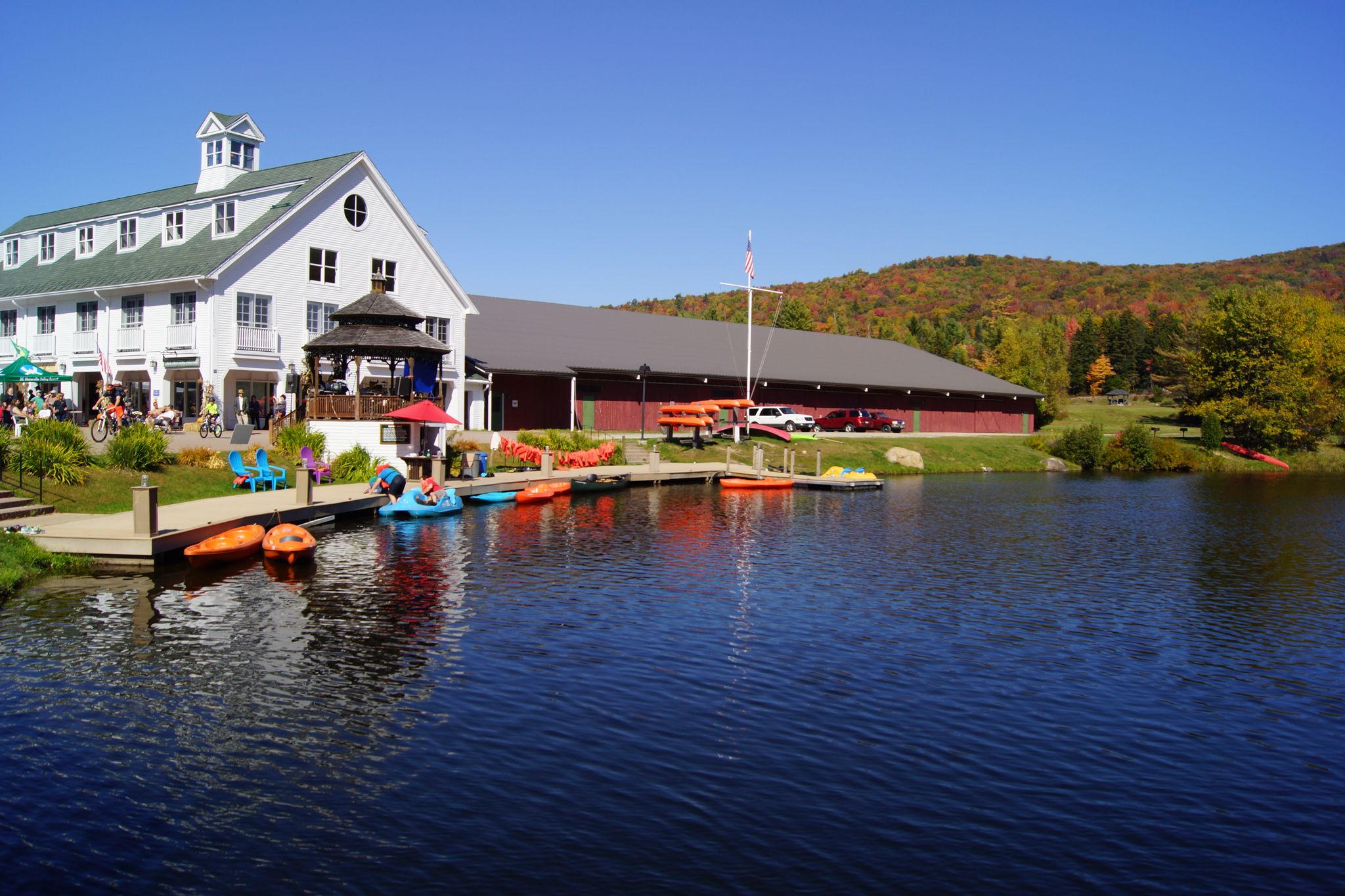People enjoy a sunny day by a lake with buildings and colorful paddle boats. - Waterville Valley and Waterville Valley Road loop gravel