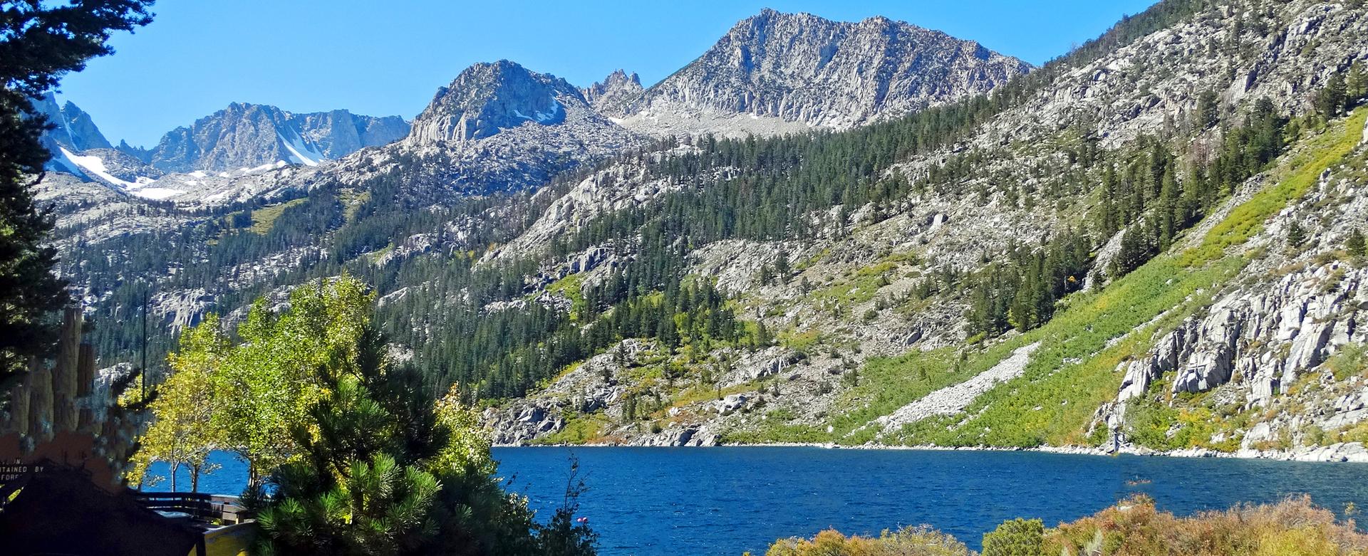Bright blue lake nestled among rocky, forested mountains under a clear sky.