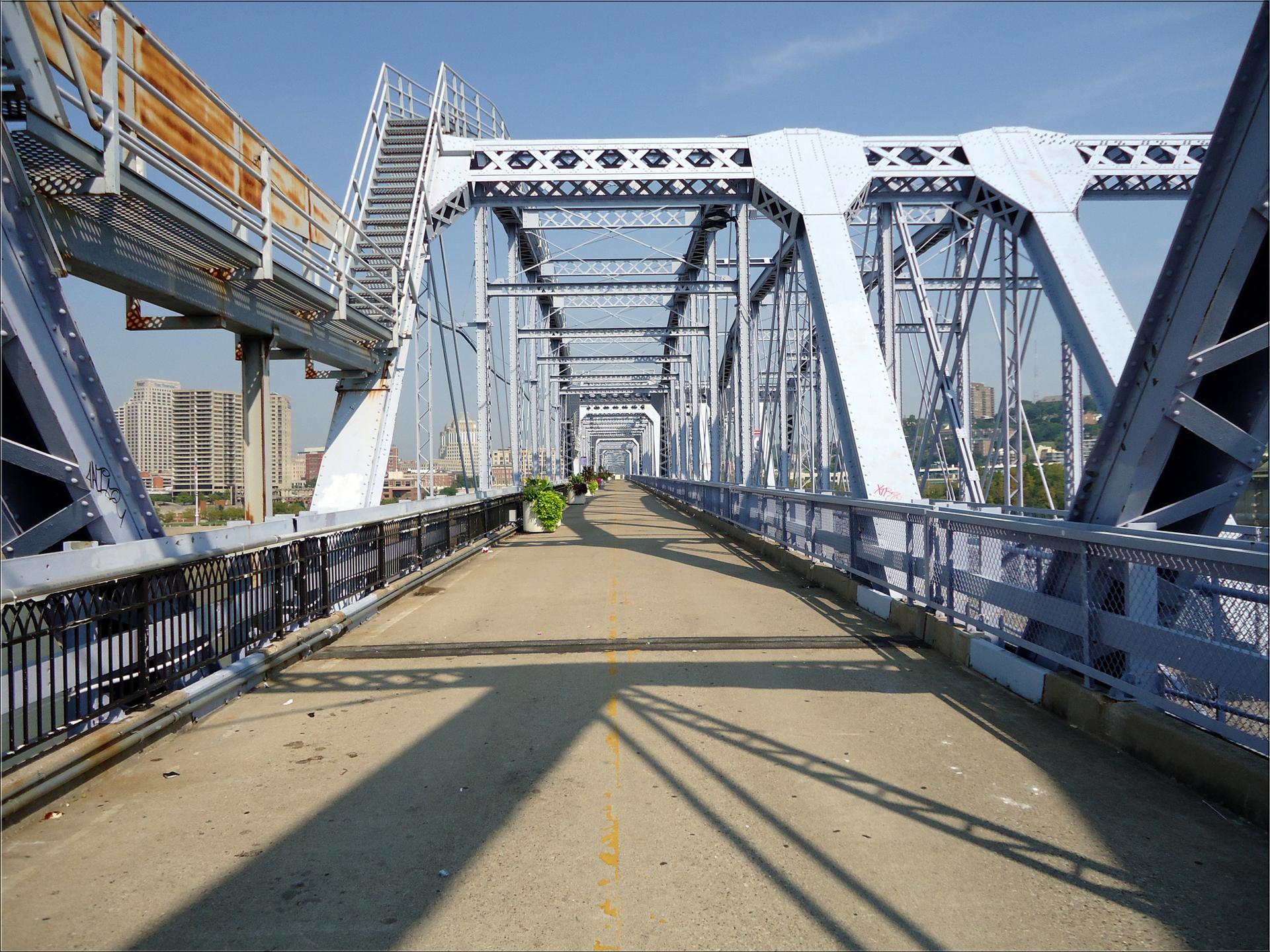 Empty pedestrian path on a large blue metal bridge under bright sun.