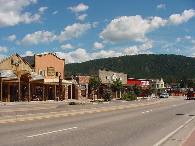 Sunny street with buildings, cars, and forested hills under a blue sky. - Mueller State Park & Divide from Woodland Park