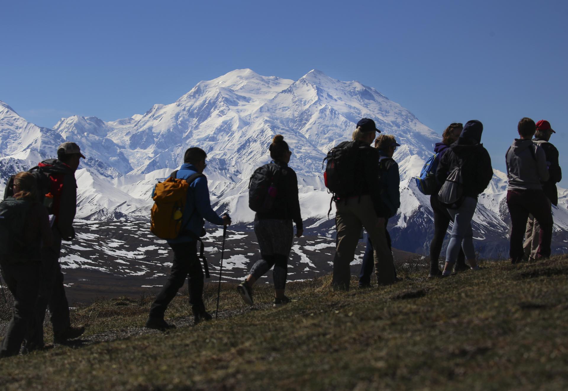 Silhouetted hikers on a ridge admiring a vast snow-covered mountain range.