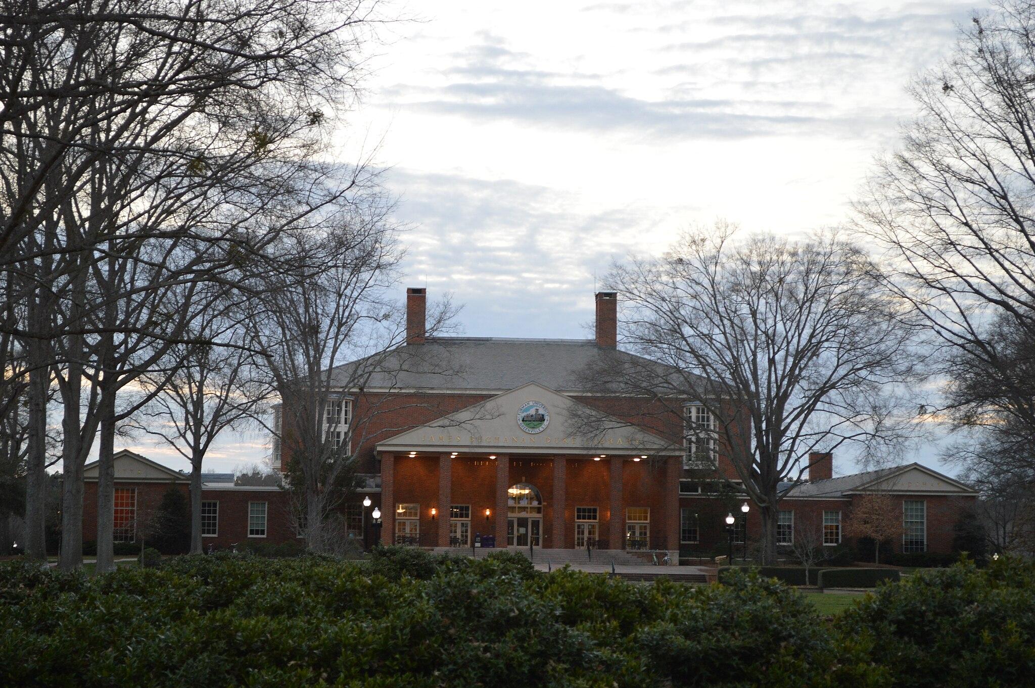 Large brick building with columns, surrounded by bare trees under an overcast sky.