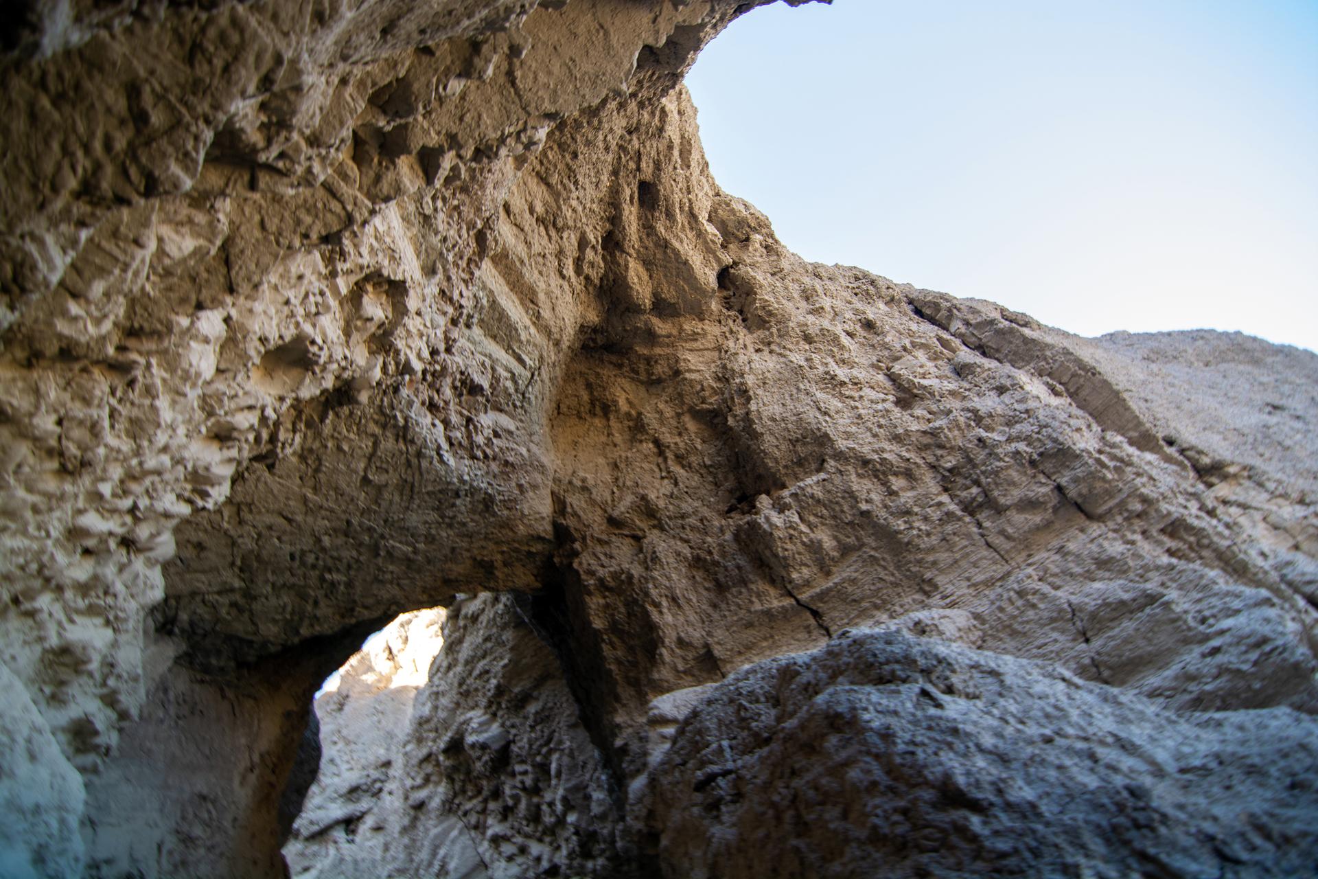Light shines through a natural rock archway in a rocky canyon.
