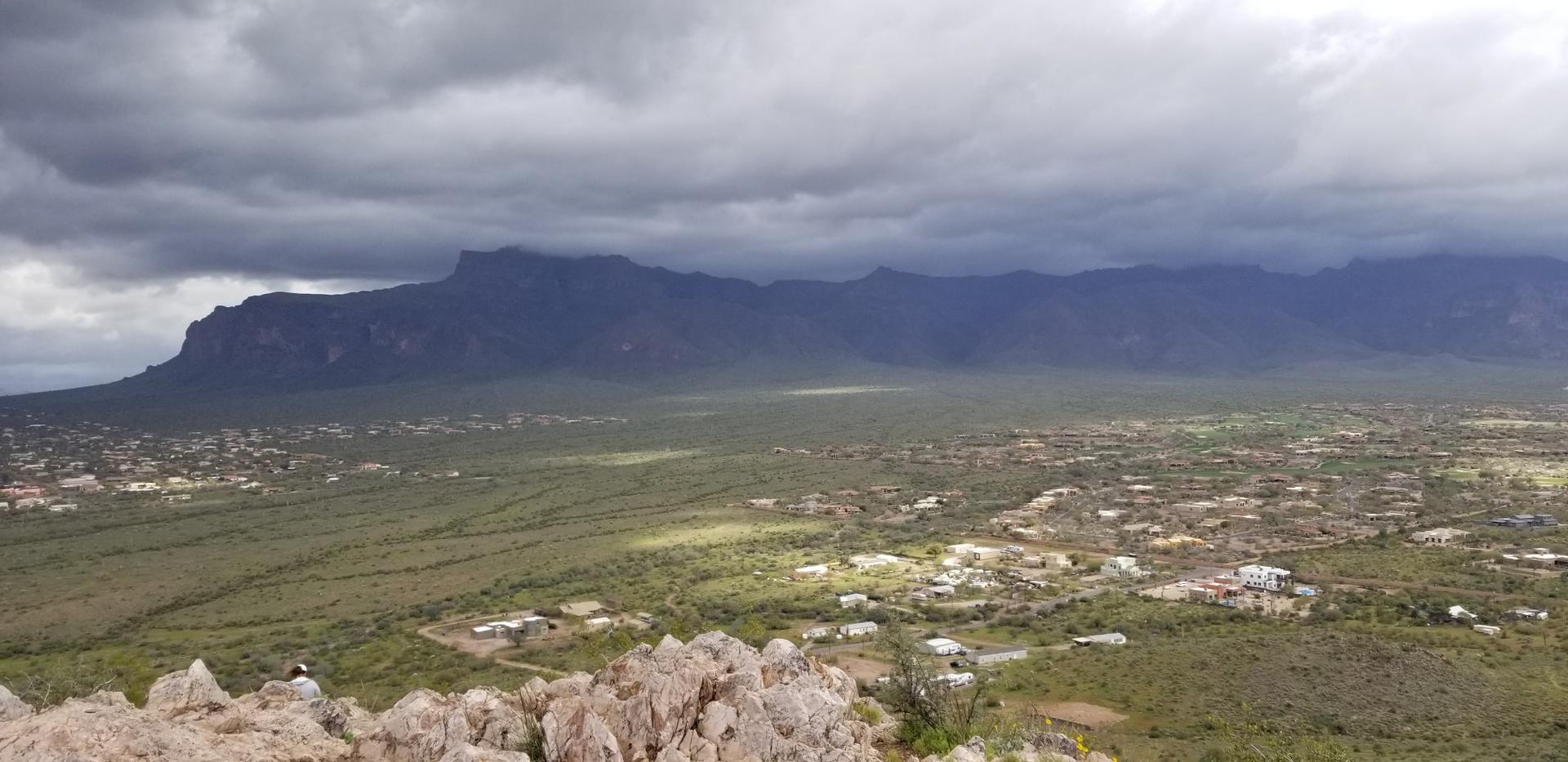 Panoramic valley view with scattered homes, dark mountains, and dramatic cloudy sky.