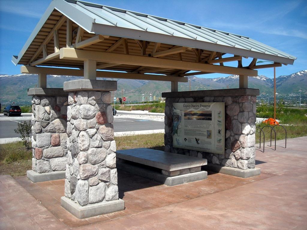 A stone and wood shelter with an informational sign and bench under bright daylight.