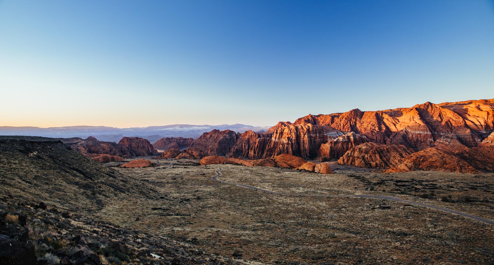 Expansive desert landscape with sunlit red rock cliffs at golden hour.