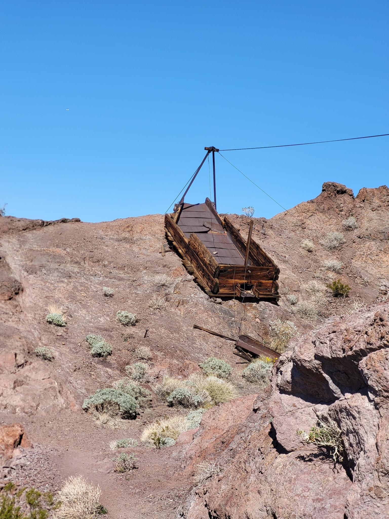 Abandoned wooden mining chute on a sunny, rocky desert slope.