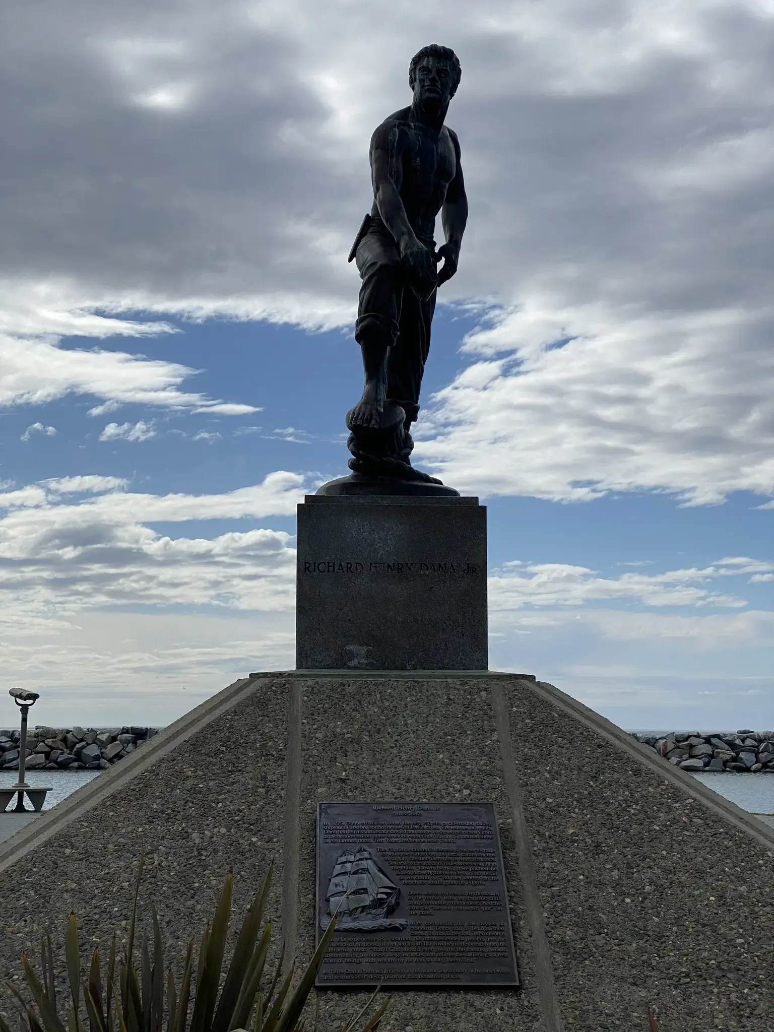 Bronze statue of a man on a pedestal under a cloudy sky.