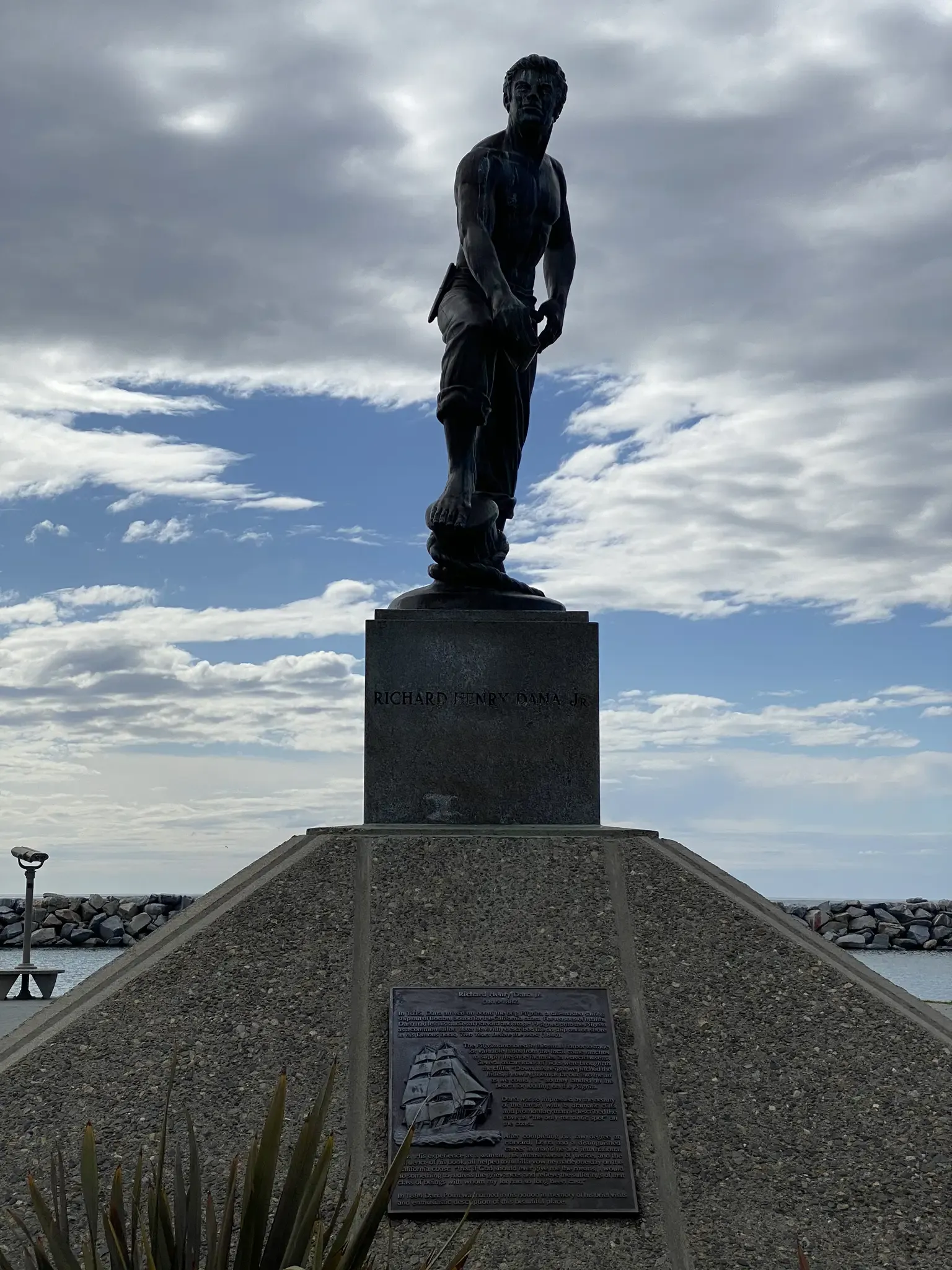 Bronze statue of a man on a pedestal under a cloudy sky. - Dana Point Harbor Trail