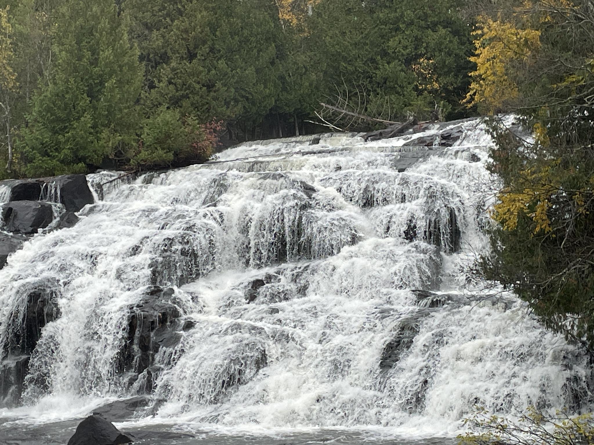 Close-up of a wide, multi-tiered waterfall with white rushing water over dark rocks.