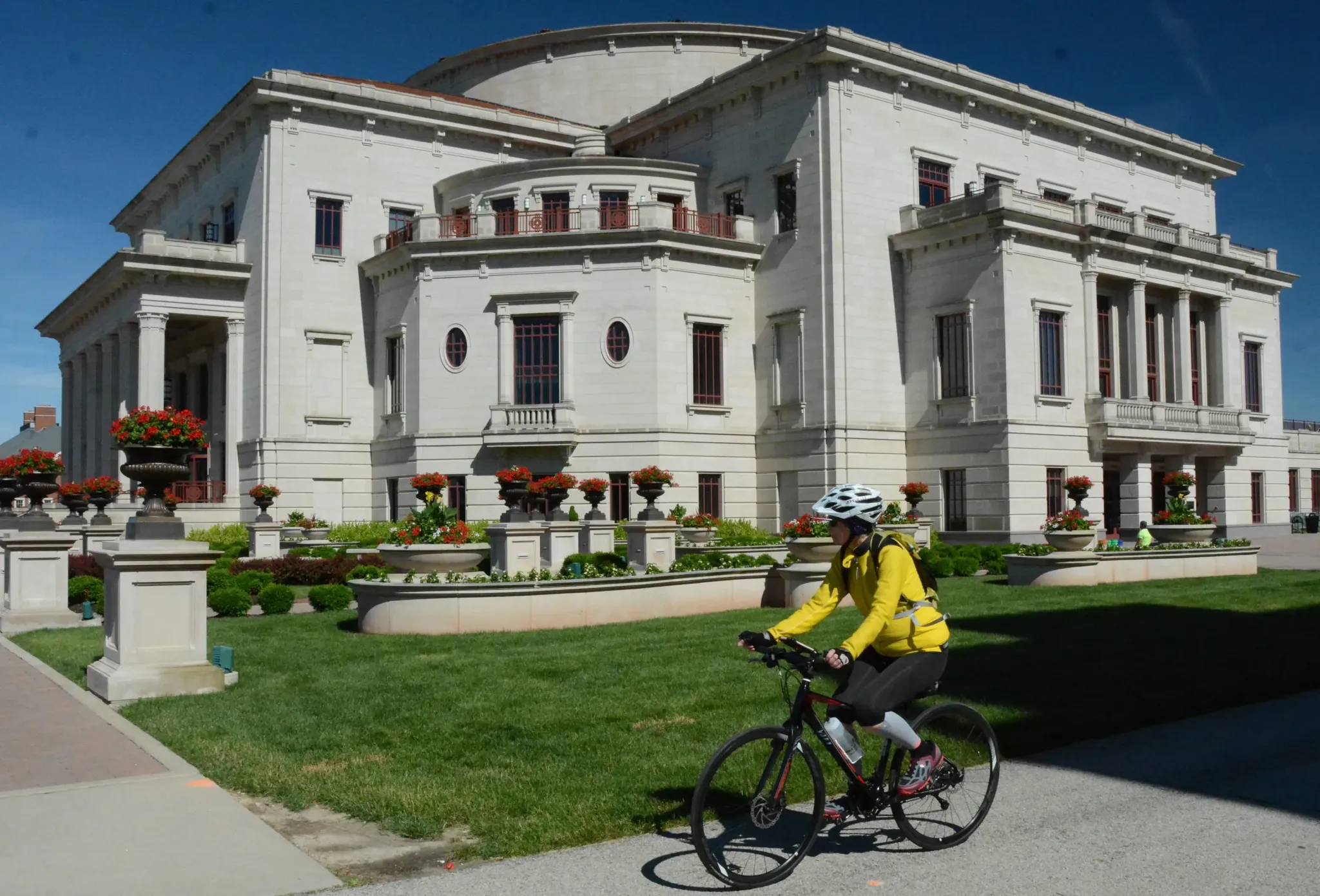 Cyclist in yellow jacket rides past a grand, light-colored building on a sunny day. - Monon Trail and USBR 35 Loop