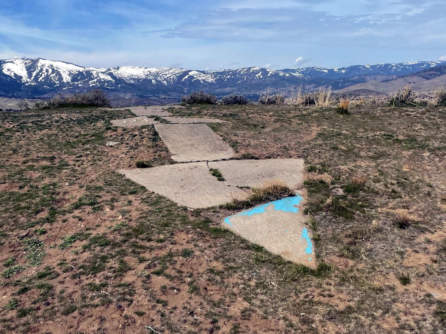 Concrete arrow on a grassy hill points towards distant snow-capped mountains.