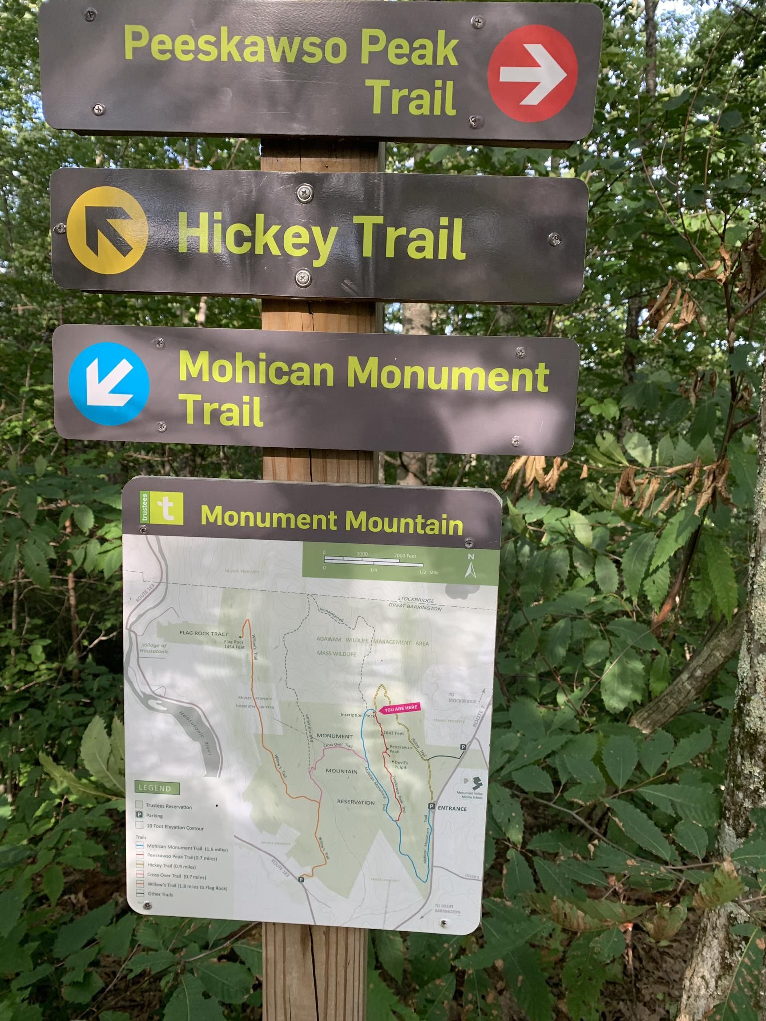 A wooden post with multiple trail signs and a map in a green forest. - Hickey and Peeskawso Peak Loop