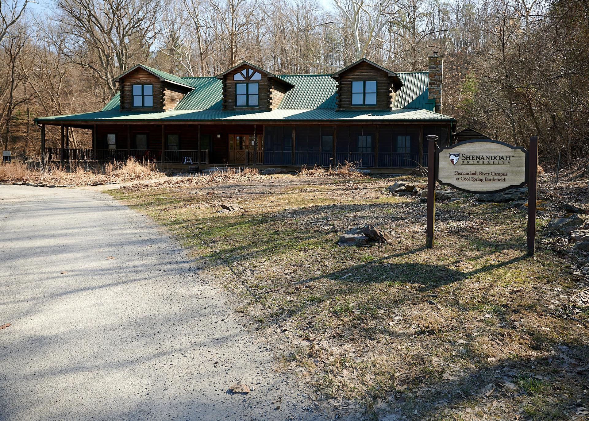 Large wooden lodge with green roof, sign, and paved path under bright daylight.