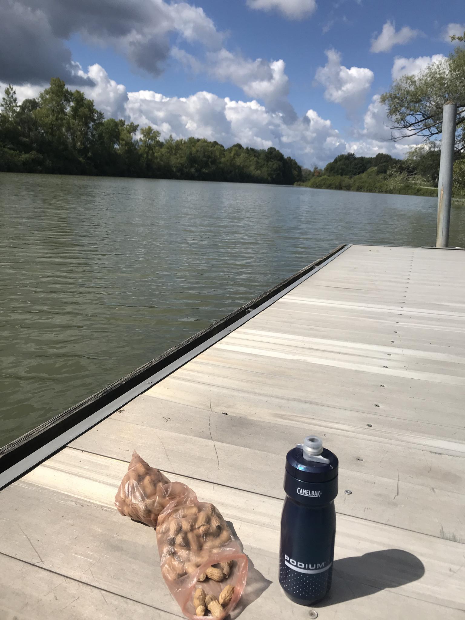 Peanuts and water bottle on a wooden dock next to a calm river.