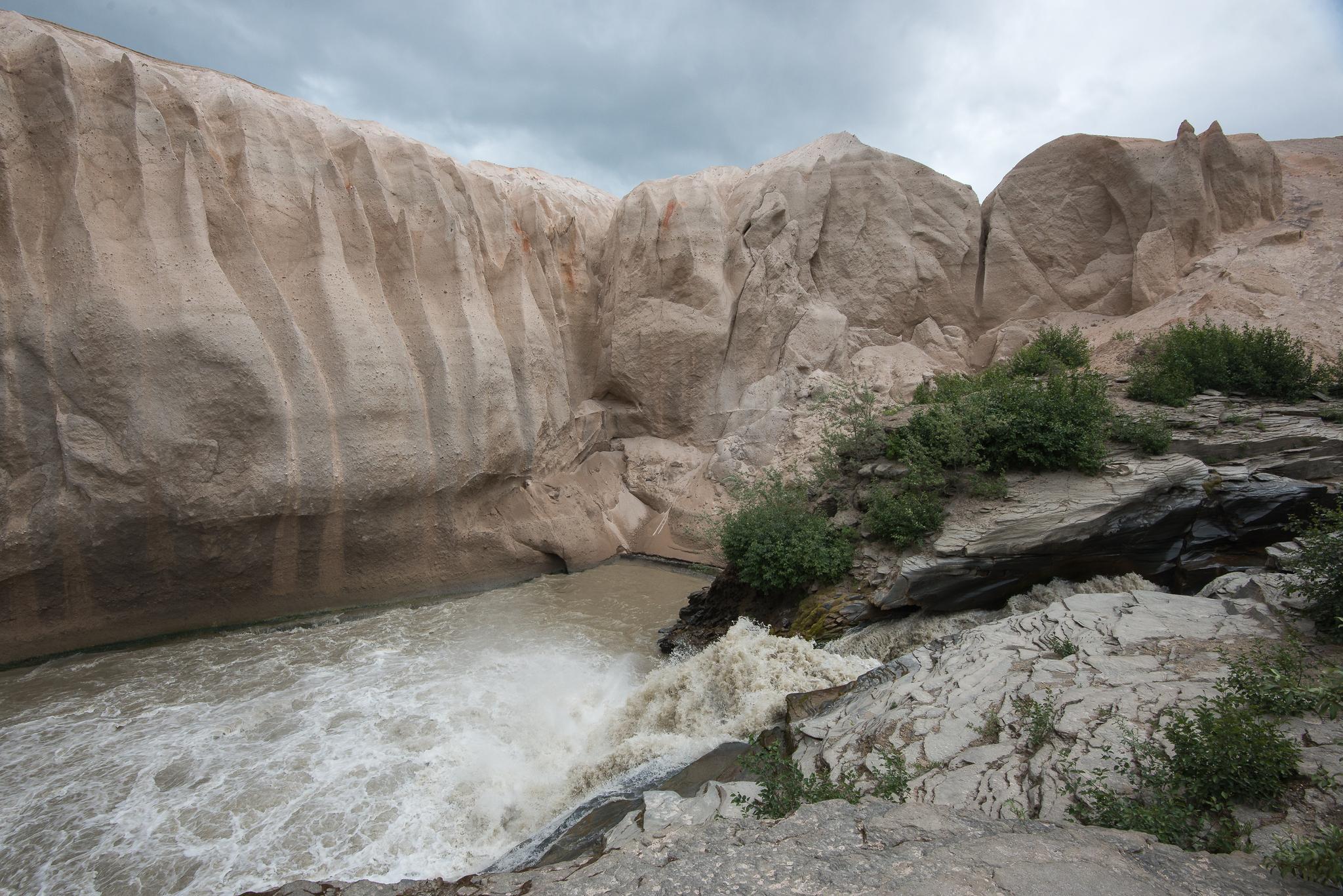 Turbulent river flows through a narrow, light-colored rock canyon under cloudy sky.
