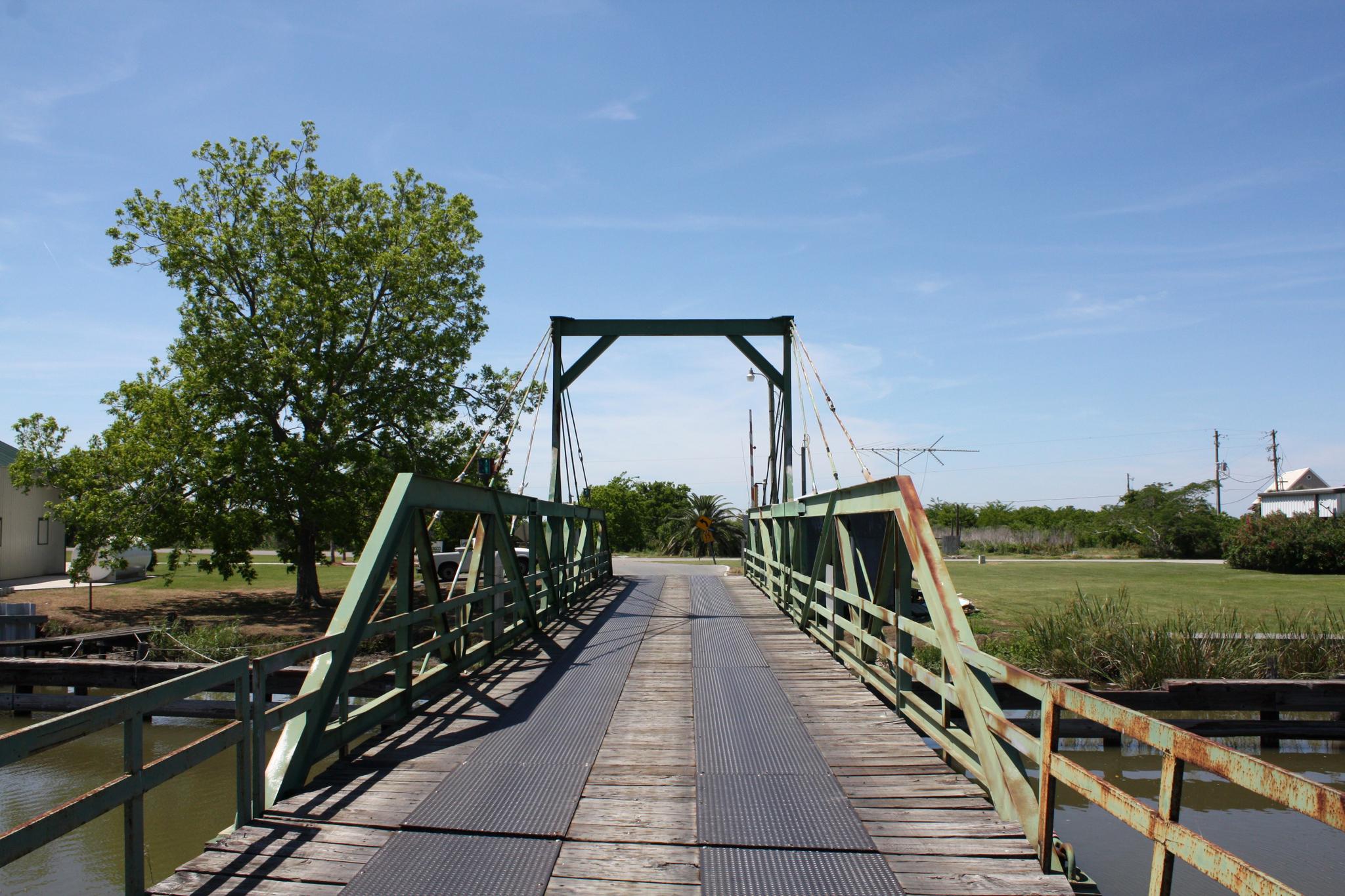 A rustic green bridge with wooden planks crosses water on a sunny day.