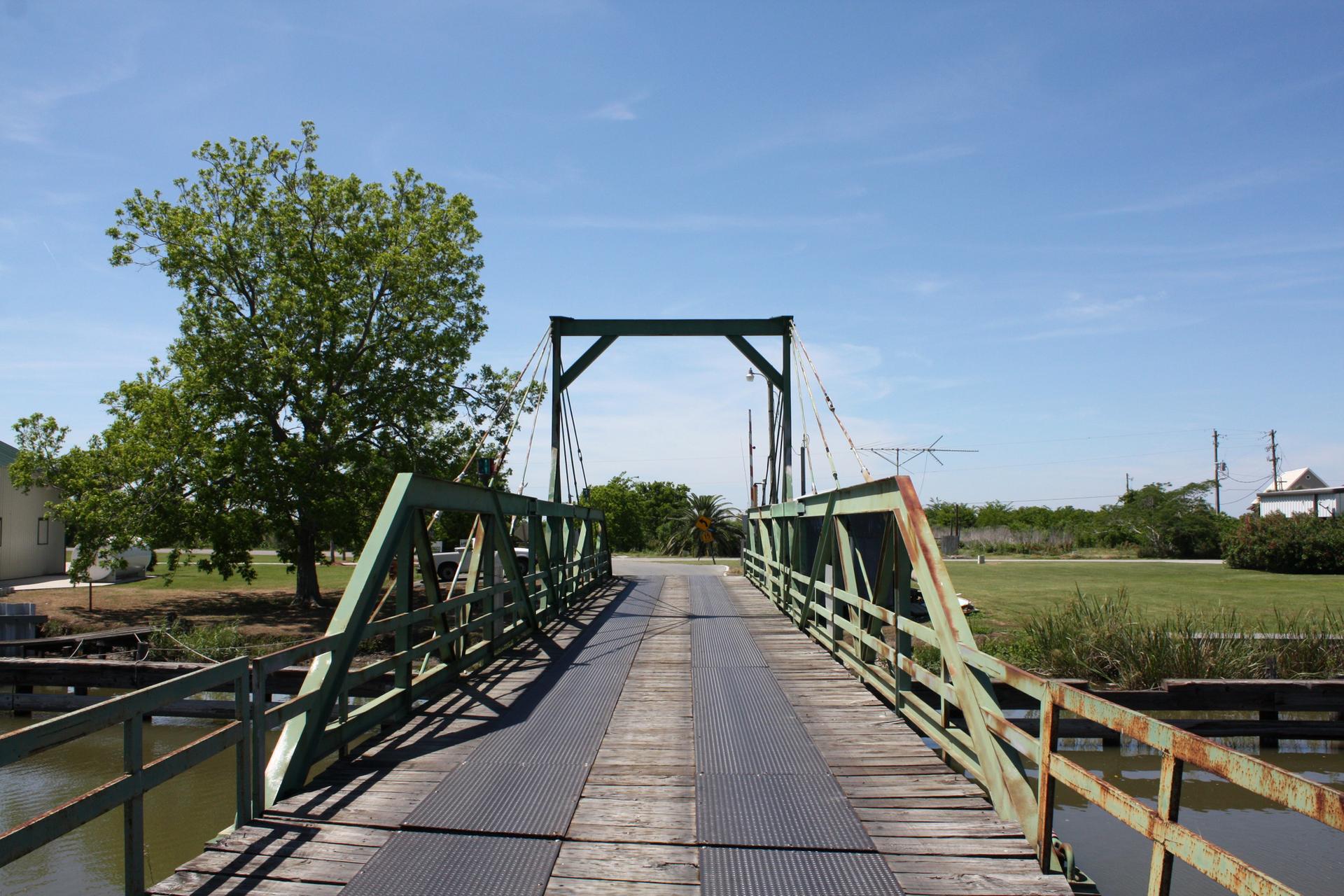 A rustic green bridge with wooden planks crosses water on a sunny day.