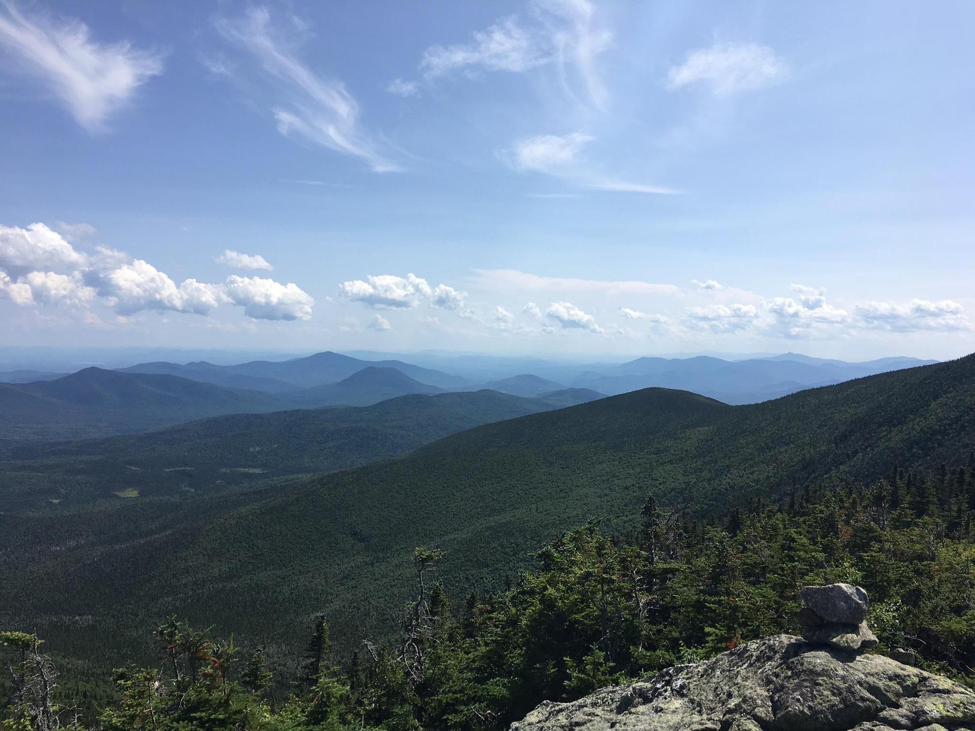 Expansive view of green forested mountains under a bright blue sky.