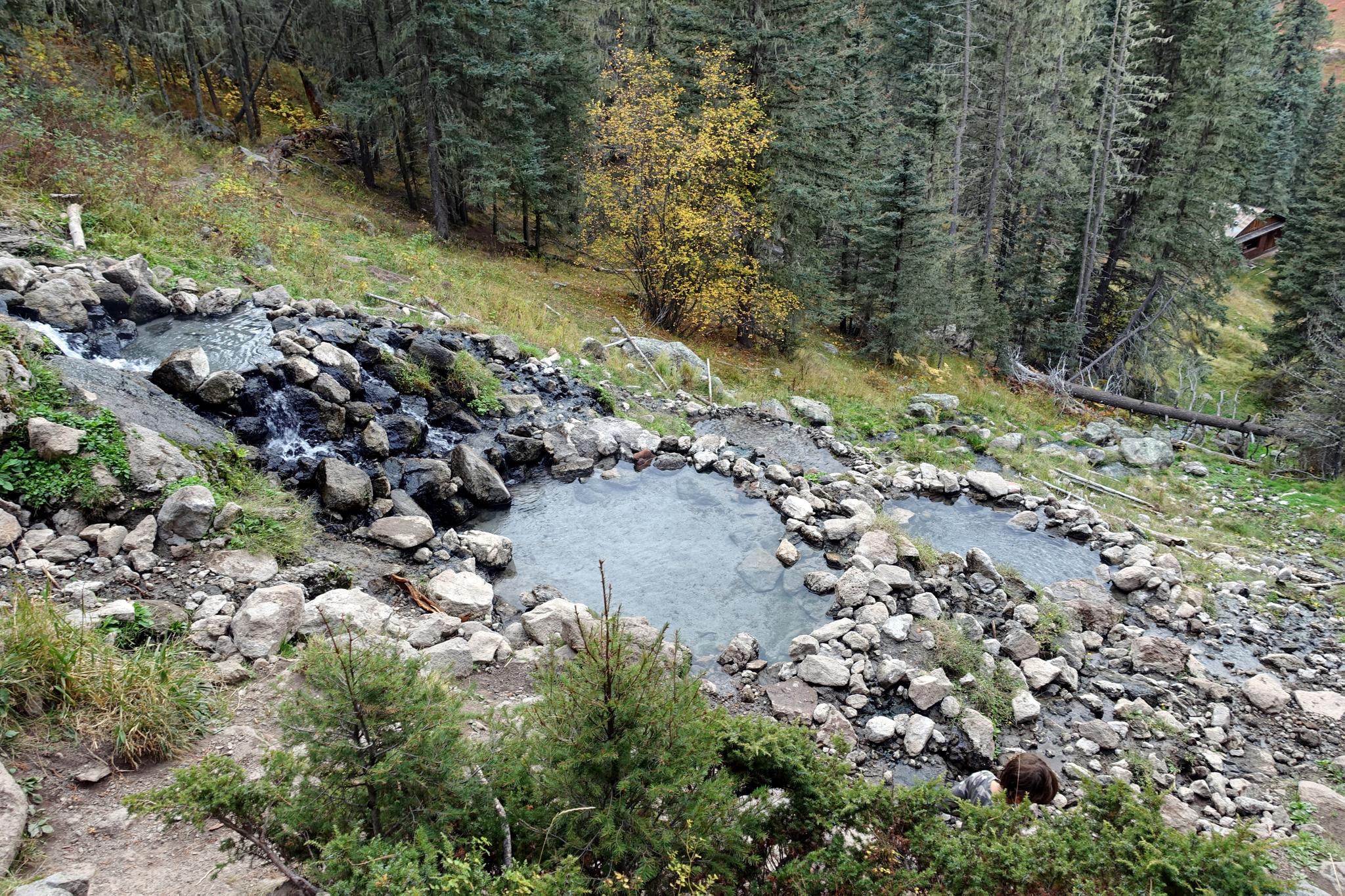 Terraced hot spring pools on a rocky, forested hillside under diffused light.