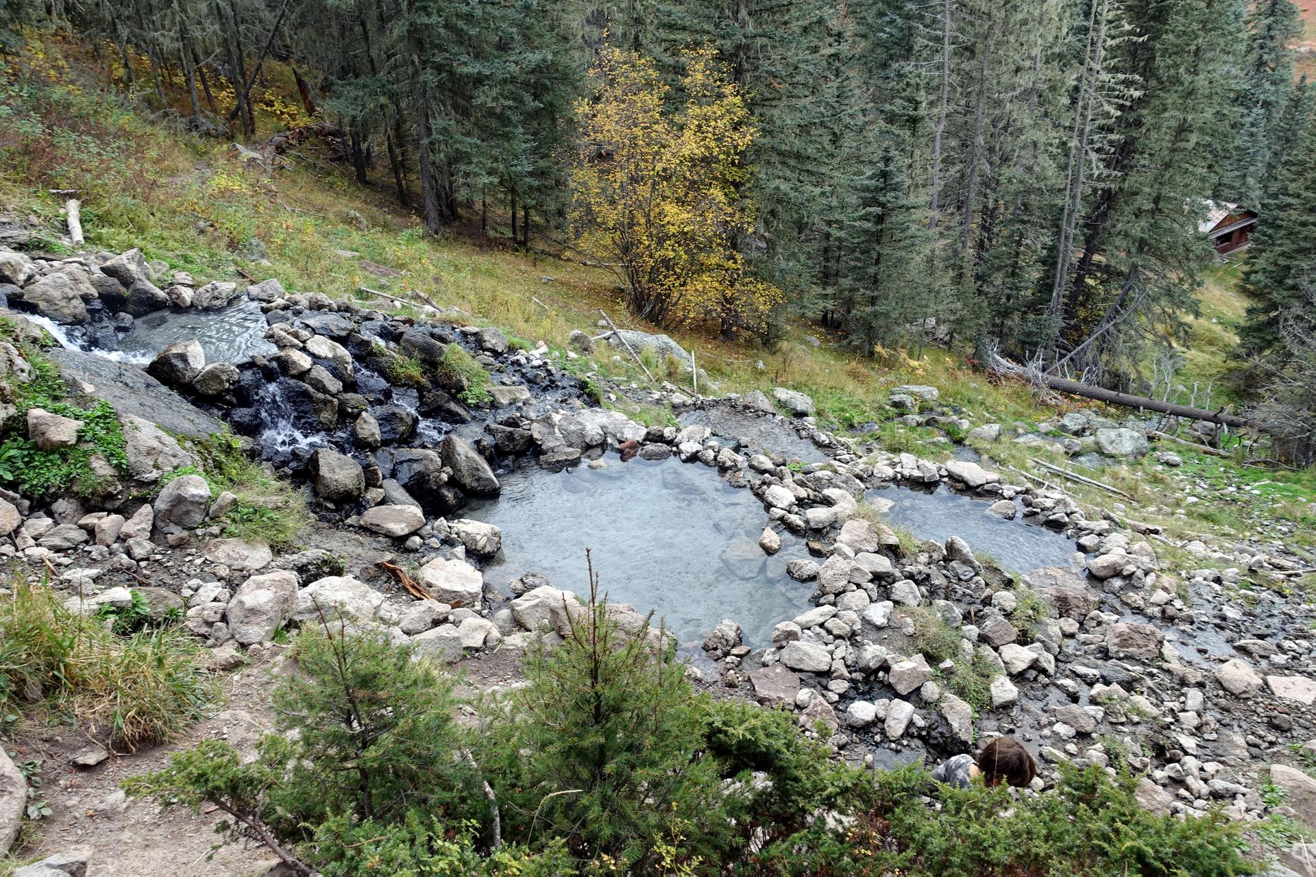 Terraced hot spring pools on a rocky, forested hillside under diffused light.
