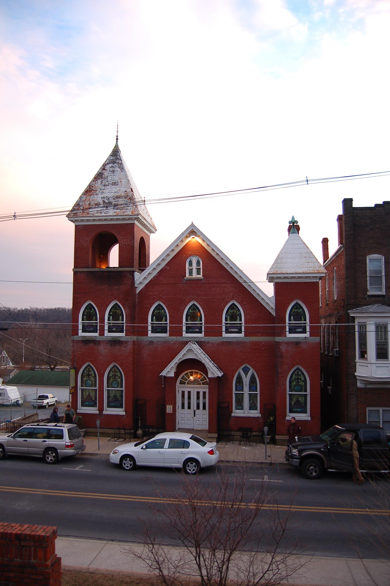 A red brick church with a steeple stands by a street at dusk.