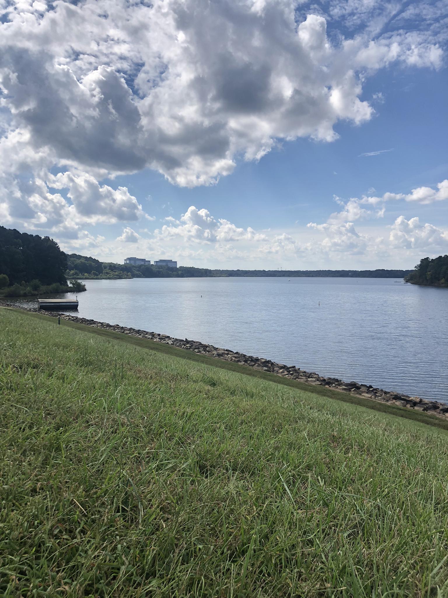 Wide lake with a grassy bank under a partly cloudy sky.